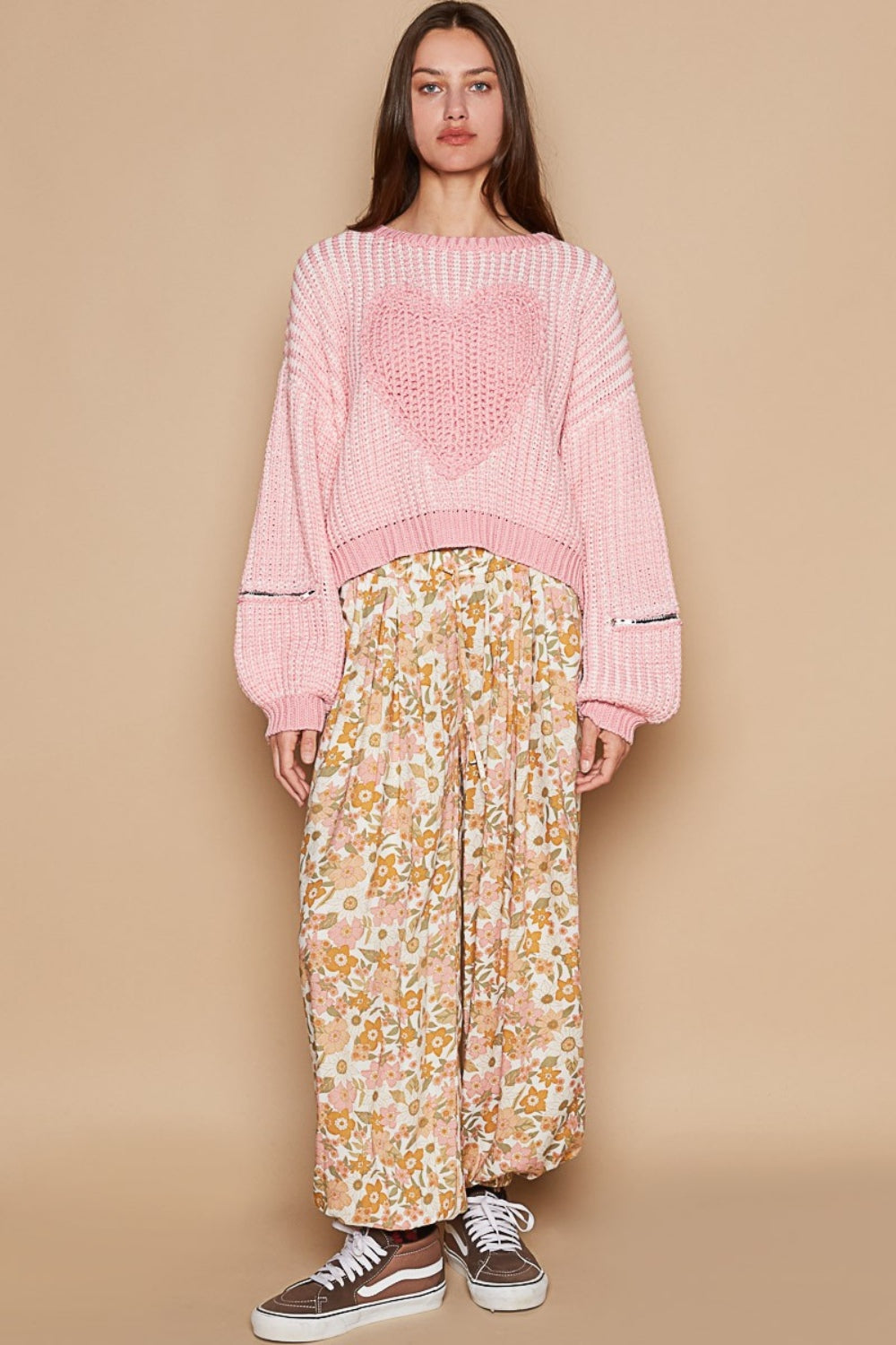 A woman wearing a playful pink POL Round Neck Heart Patch Zipper Point Sleeve Sweater and a floral skirt stands against a plain background.