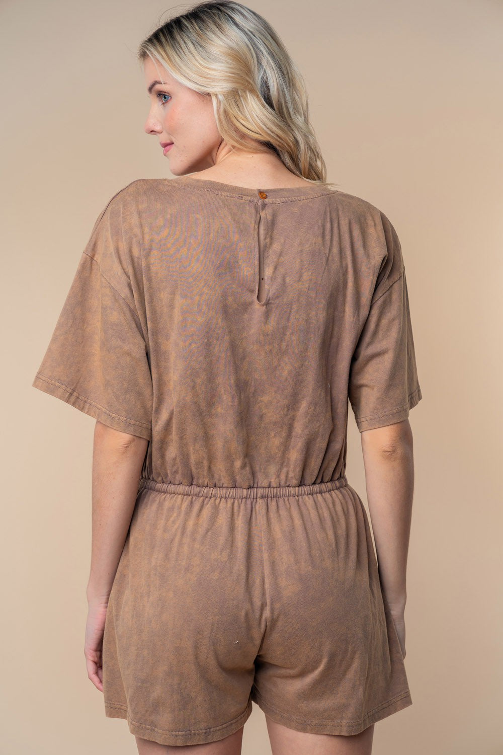 A person wearing the White Birch Full Size Short Sleeve Drawstring Romper stands against a beige background, looking slightly to the side. Perfect for your summer wardrobe, this stylish ensemble is both comfortable and chic in a cotton knit texture.