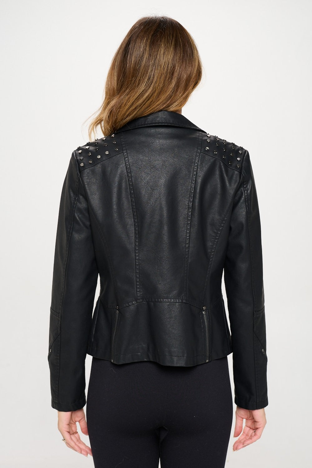 Clad in a Coalition LA Studded Classic Moto Faux Leather Jacket featuring an asymmetrical zipper closure, along with black athletic wear, an individual strikes a pose against a plain white background, radiating an edgy flair.