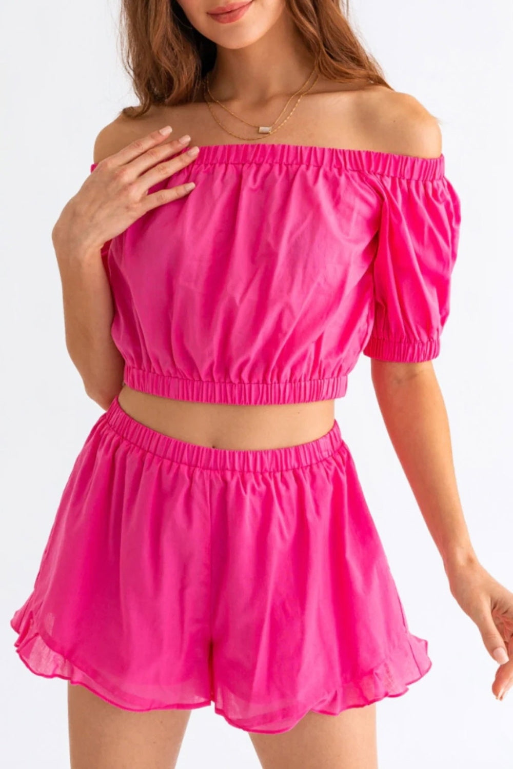 Person wearing the Le Lis Off Shoulder Crop Top and Ruffled Shorts Set, featuring a bright pink, off-the-shoulder crop top with puffed sleeves paired with matching high-waisted ruffled shorts, the perfect summer outfit.