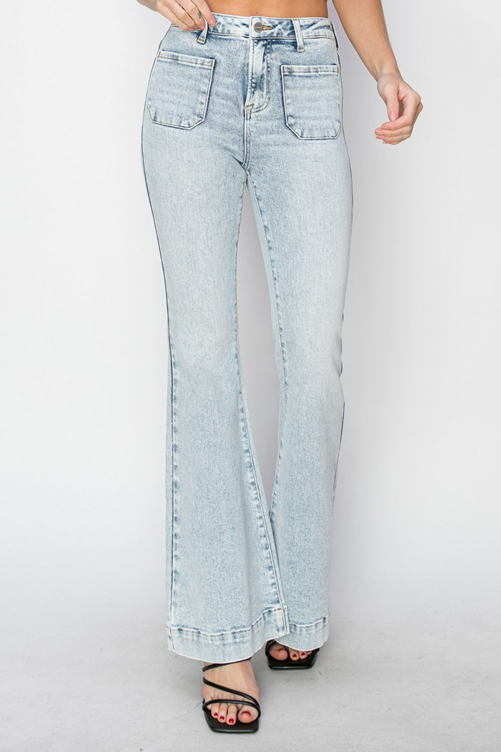A person wearing Risen Full Size High Rise Front Patch Pocket Flare Jeans in a light wash, paired with black strappy sandals, stands against a white background.