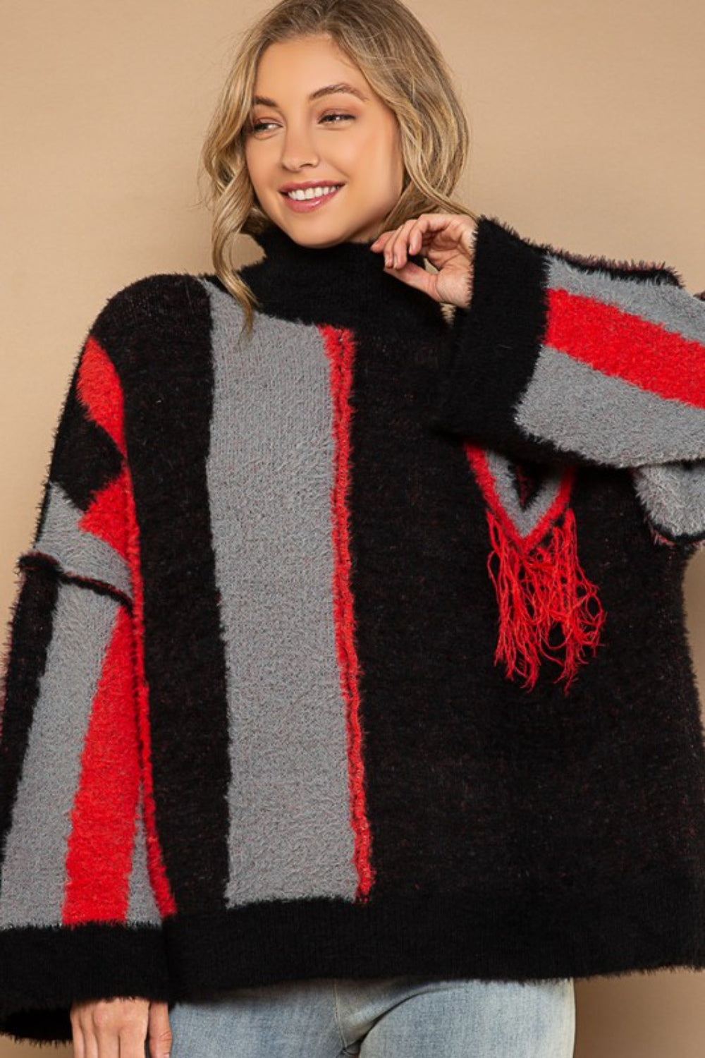 A person with long hair smiles while wearing the chic POL Turtleneck Color Block Fringe Detail Sweater in black, red, and gray.