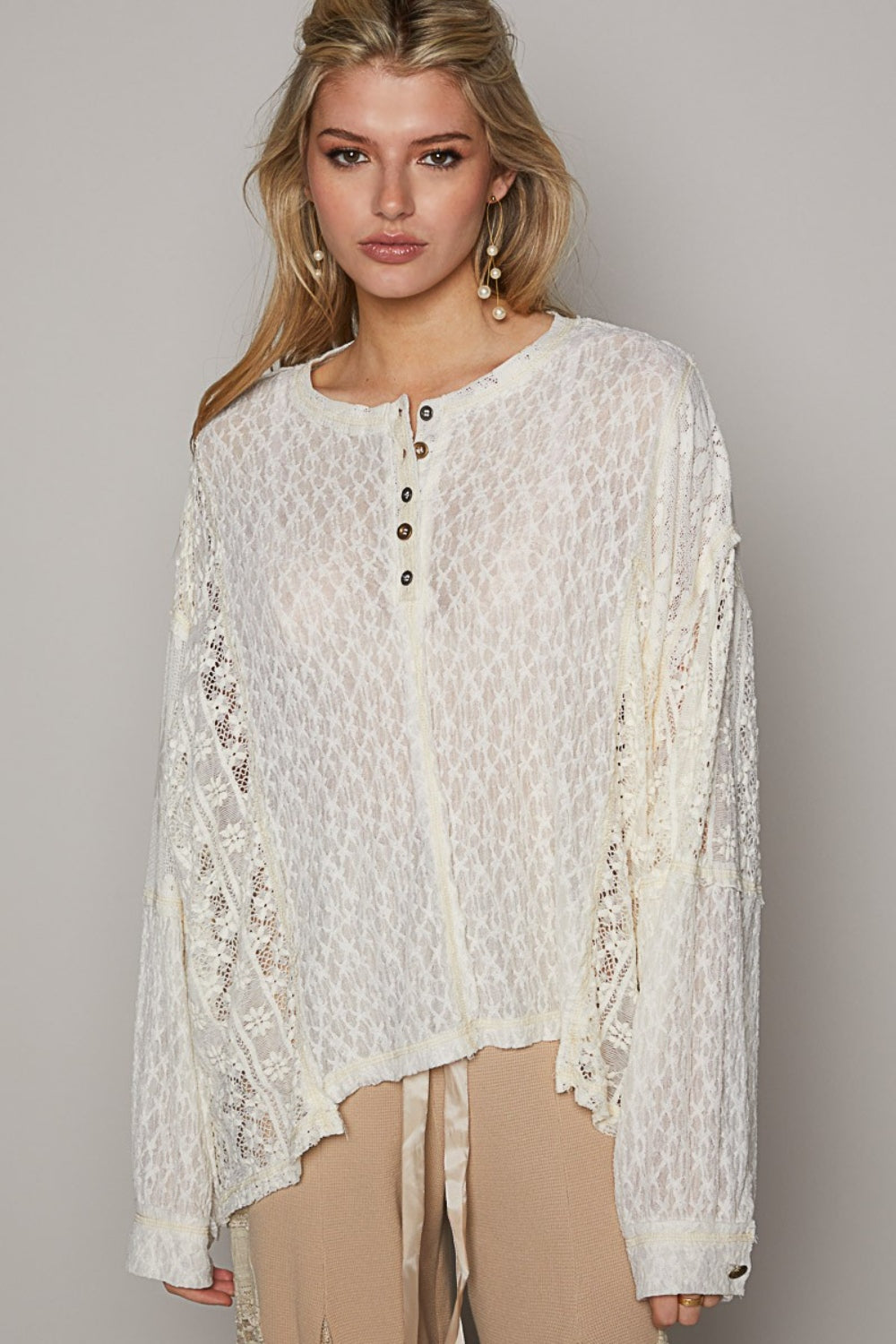 A woman is wearing the POL Round Neck Long Sleeve Raw Edge Lace Top, paired with beige pants, as she stands against a neutral background.