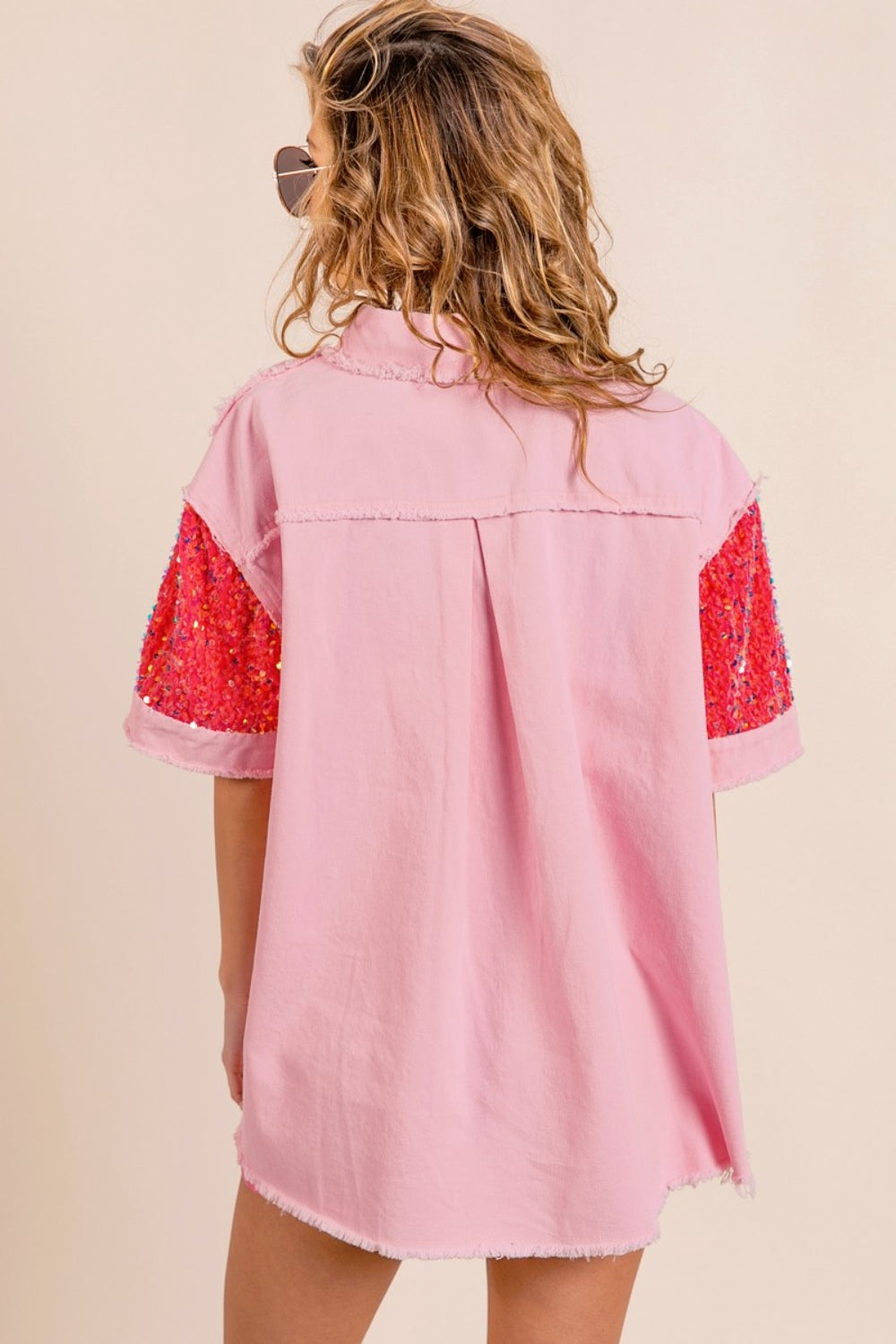 A woman poses in the BiBi Sequin Detail Raw Hem Short Sleeve Shirt, a pink button-up with red sequin detail pockets, paired with matching pink shorts and reflective aviator sunglasses.