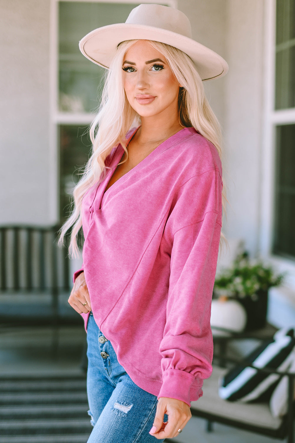 A woman stands with her back to the camera, wearing a long-sleeved Rose Exposed Seam Twist Open Back Oversized Sweatshirt and light blue jeans, showcasing a relaxed fit.