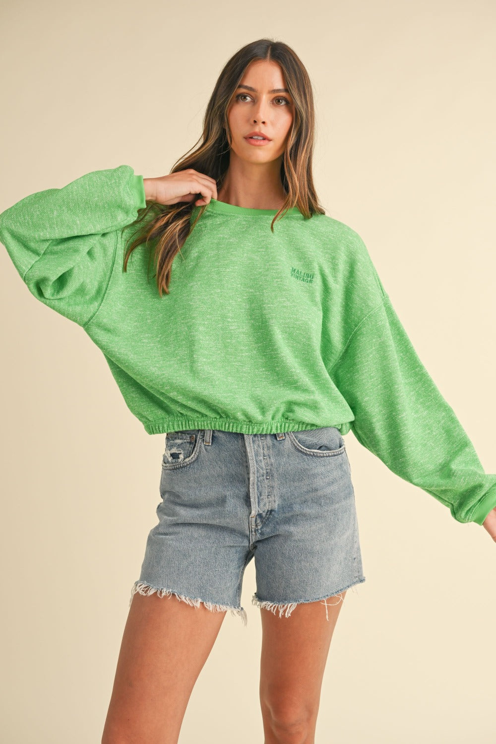 A woman models a Mable Round Neck Letter Embroidery Crop Sweatshirt in green, paired with denim shorts, against a plain background, effortlessly showcasing her street style.