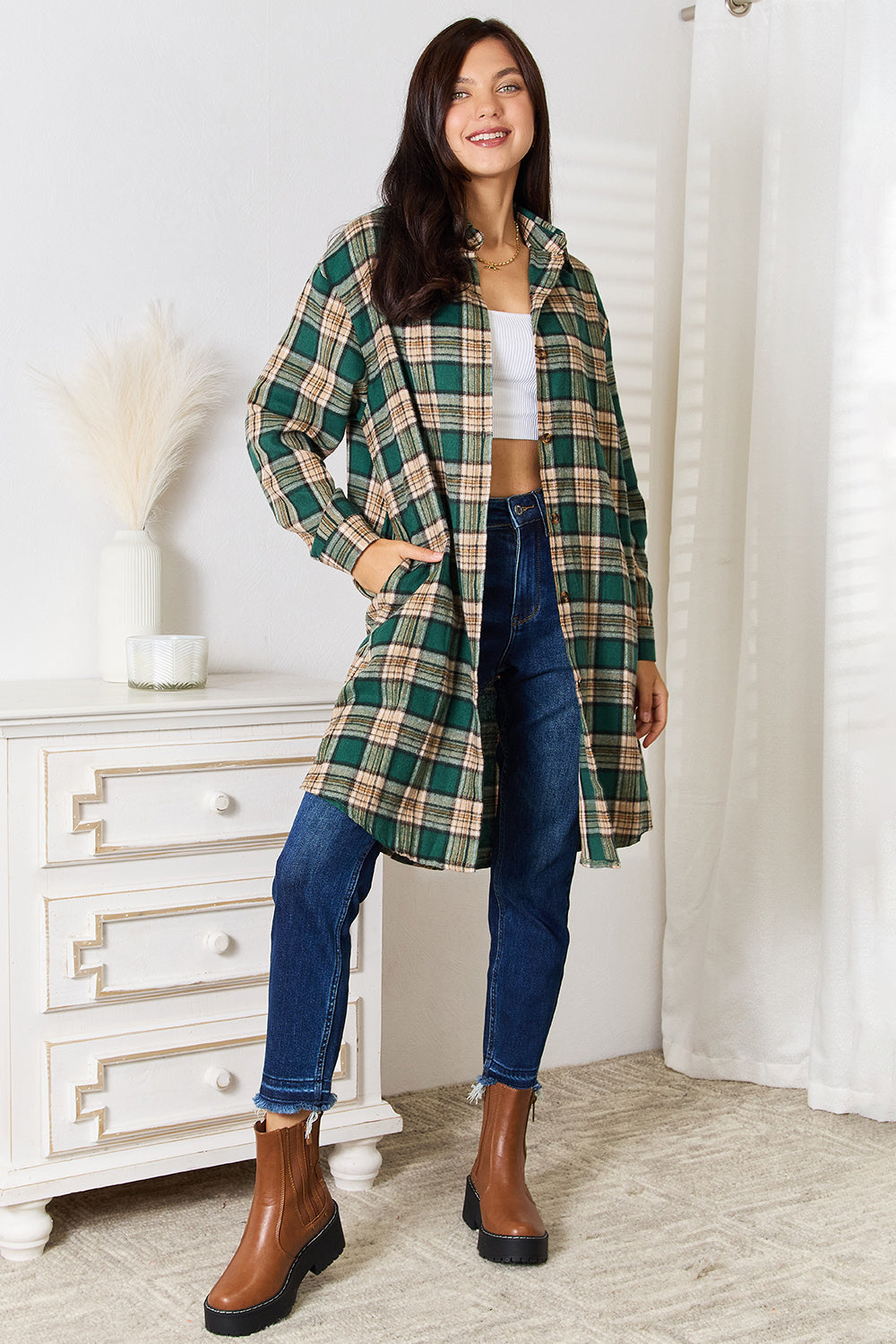 A person wearing the Mandy Plaid Collared Neck Long Sleeve Shirt in green and beige over a white crop top and blue jeans, standing indoors near a white dresser with vases.