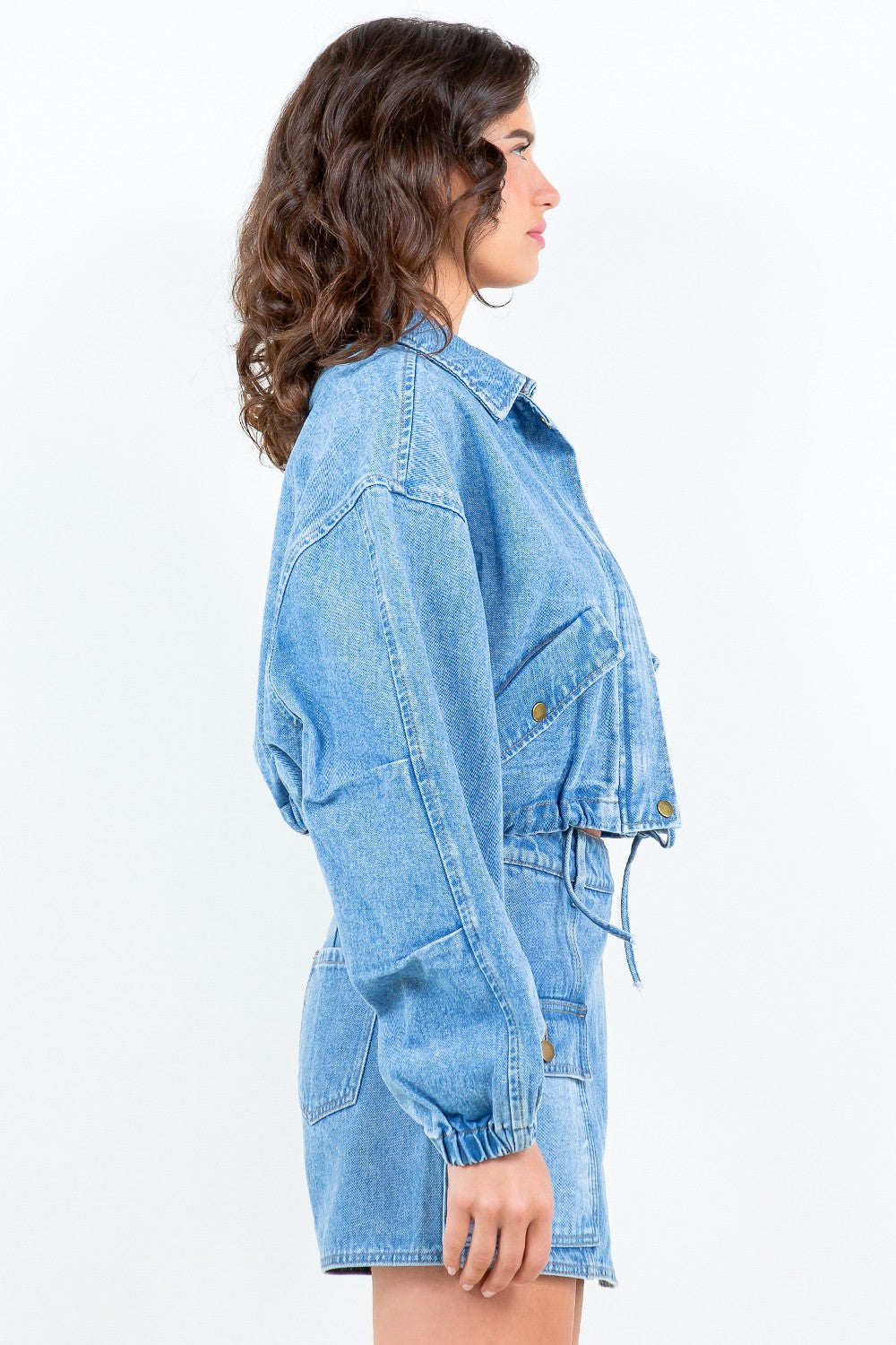 A woman wearing the American Bazi Drawstring Waist Crop Denim Jacket in light blue denim and a matching skirt, standing against a plain light background.