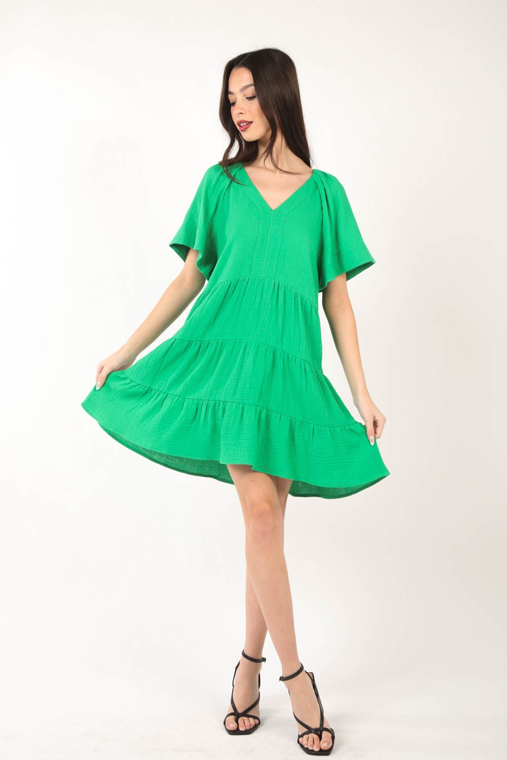 A woman poses against a white background, elegantly showcasing the flattering silhouette of the VERY J Texture V-Neck Ruffled Tiered Dress.