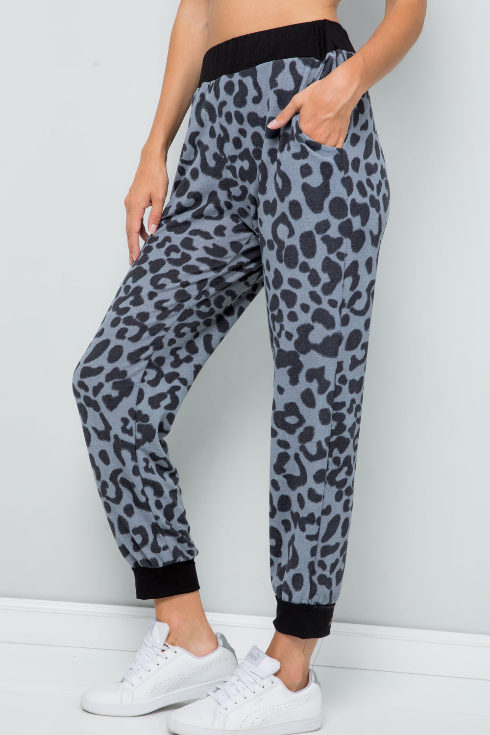 Person wearing Celeste Full Size Leopard Contrast Sweatpants with a black waistband and cuffs, paired with white sneakers, against a plain light gray background.