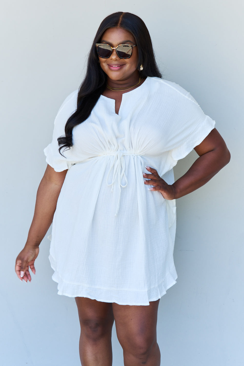 A person with long dark hair smiles while posing in the Ninexis Out Of Time Full Size Ruffle Hem Dress with Drawstring Waistband in White against a plain background.