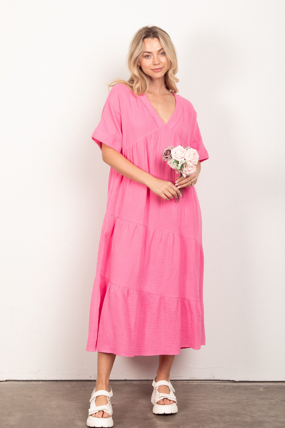 Dressed in the VERY J Soft Crinkle Gauze Short Sleeve Midi Dress in vibrant pink, a person holds a bouquet of flowers, effortlessly capturing summer style against a plain background.