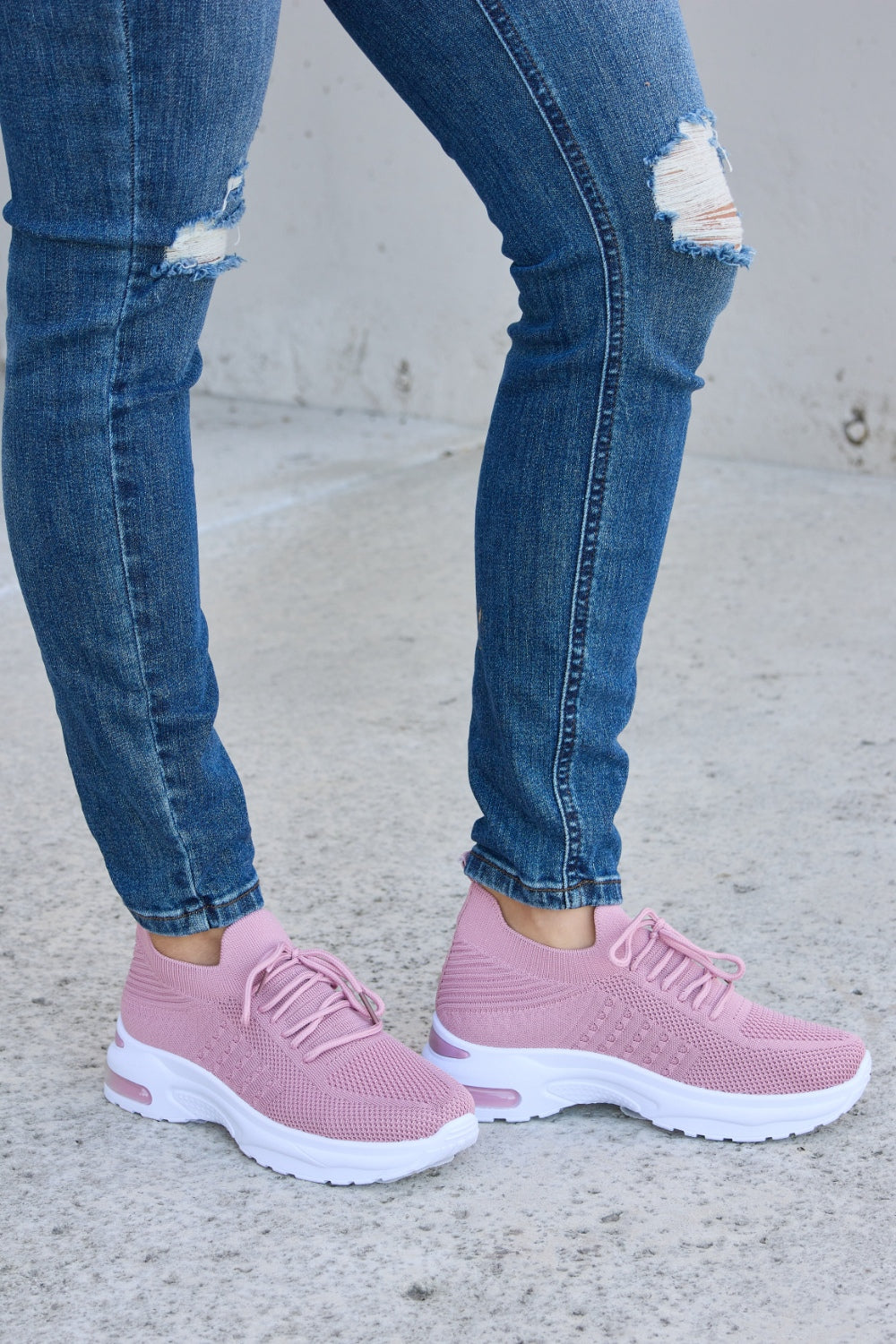 A person is wearing ripped blue jeans and Forever Link breathable mesh lace-up round toe athletic shoes, standing on a concrete surface.