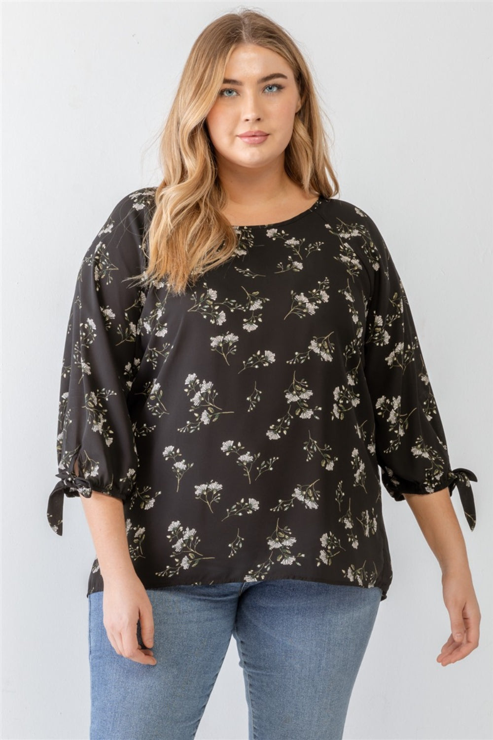 A person wearing a Zenobia Plus Size Floral Round Neck Blouse and blue jeans stands against a plain background.