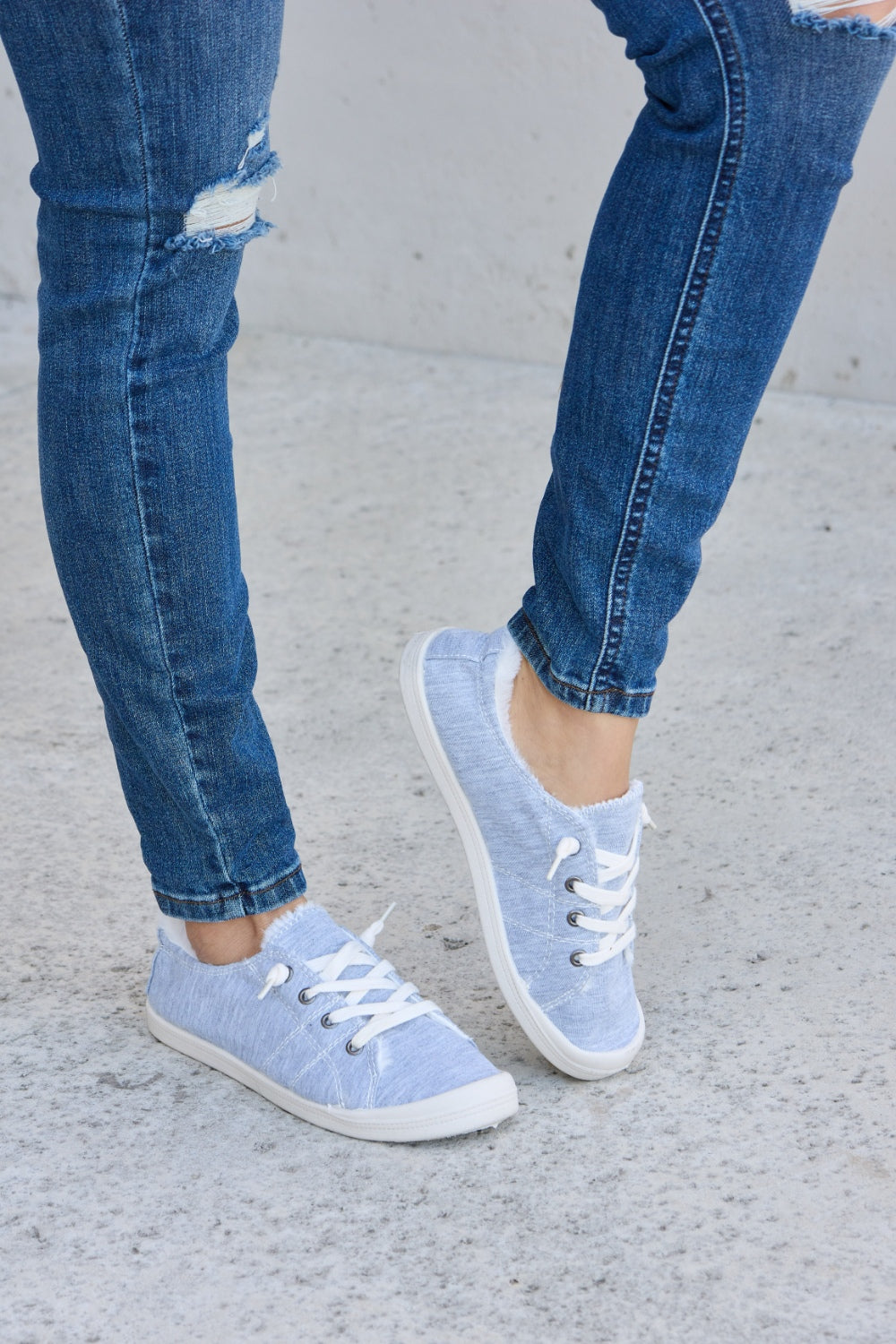 Person wearing ripped blue jeans and Forever Link Lace-Up Plush Thermal Flat Sneakers in grey with white laces, standing on a concrete surface.