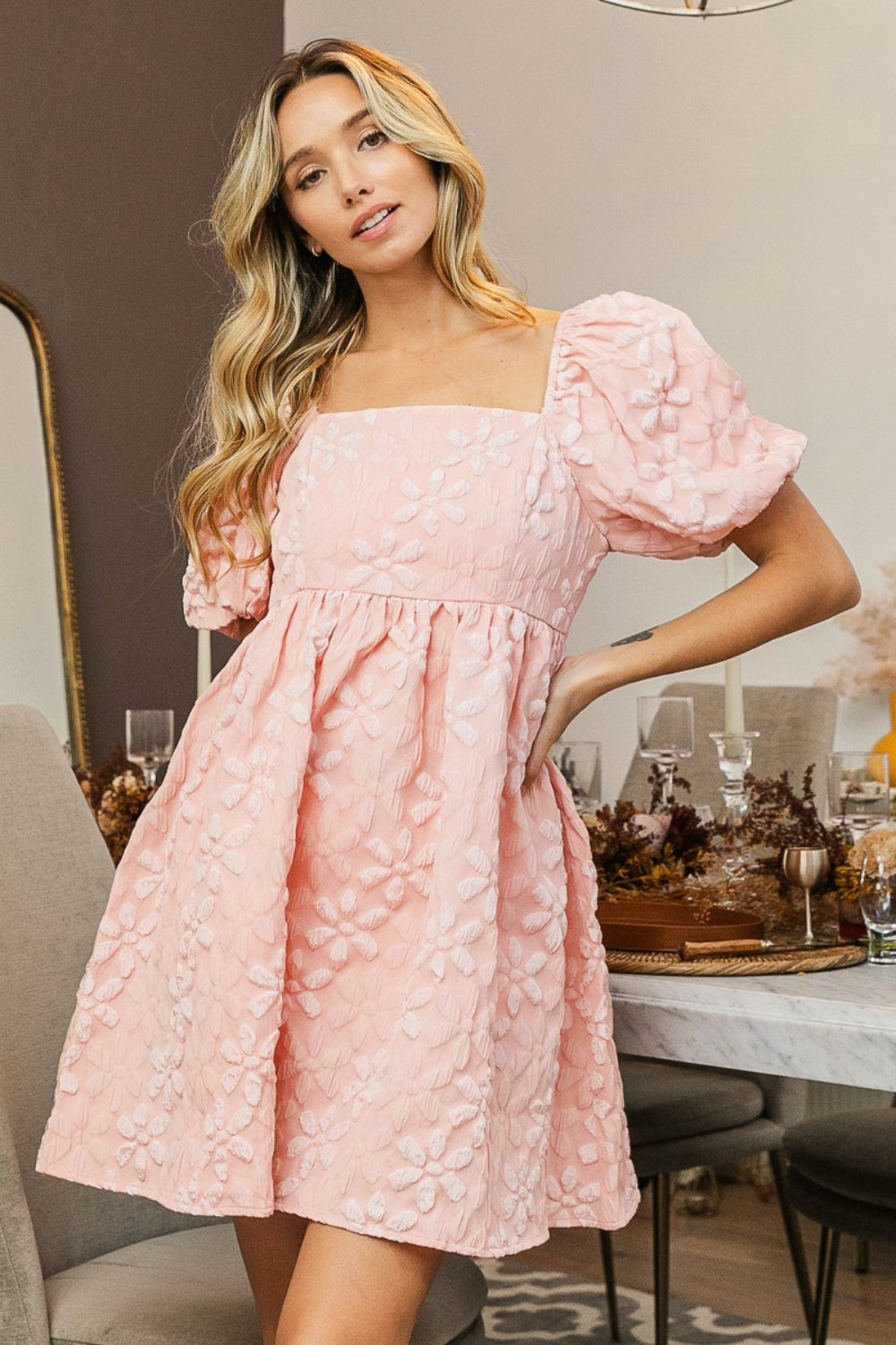 A woman in the BiBi Flower Square Neck Puff Sleeve Dress stands indoors near a set dining table, showcasing its romantic and feminine floral details.