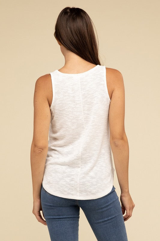 A woman in a stylish and adaptable V Neck Sleeveless Cami Top paired with jeans stands against a beige background. She has long brown hair and maintains a neutral expression.