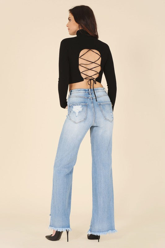 A woman wearing a stylish black mock neck lace-up open back top, paired with light blue ripped jeans.