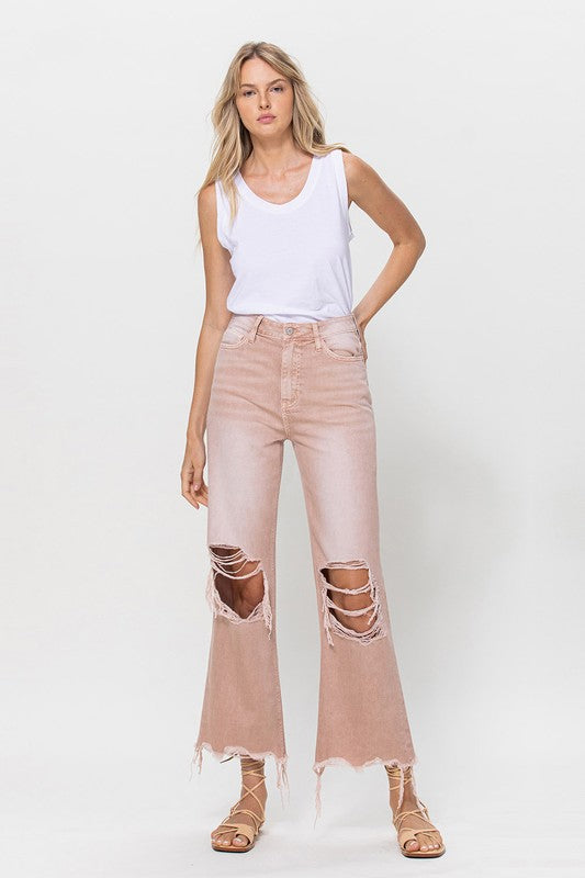 Person wearing 90's Vintage Crop Flare Jeans in rose pink with high waist, distressed details, rips on the knees, and frayed hems, paired with beige strappy sandals.