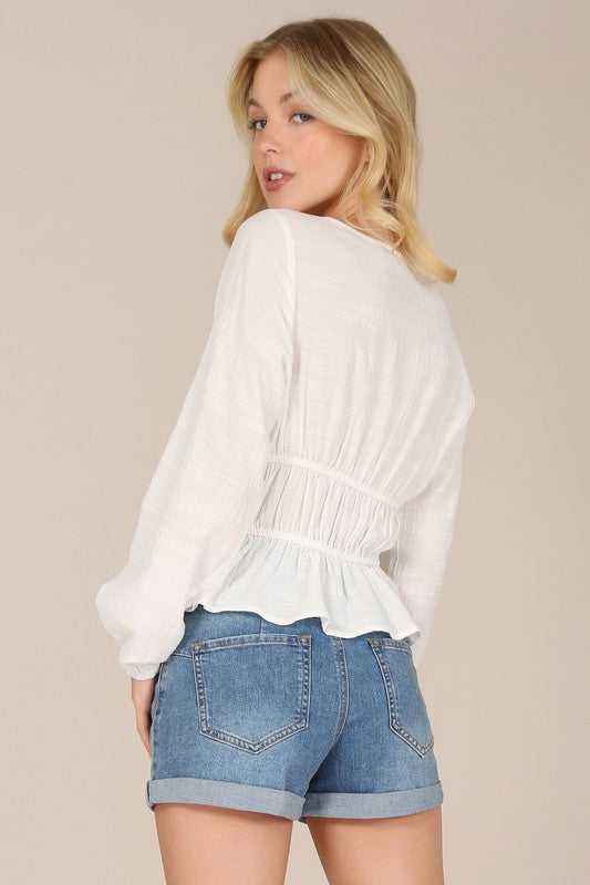 A person wearing the LS sheer lace top with long sleeves and denim shorts stands against a beige background.