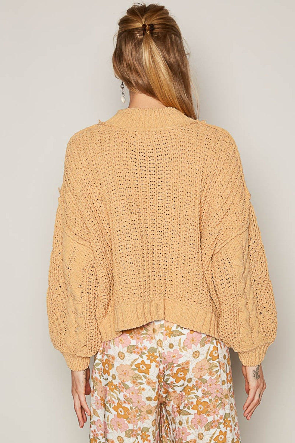 Woman with long blonde hair, smiling and standing against a plain background while wearing the POL Mock Neck Cable Knit Sweater in beige and a floral skirt.