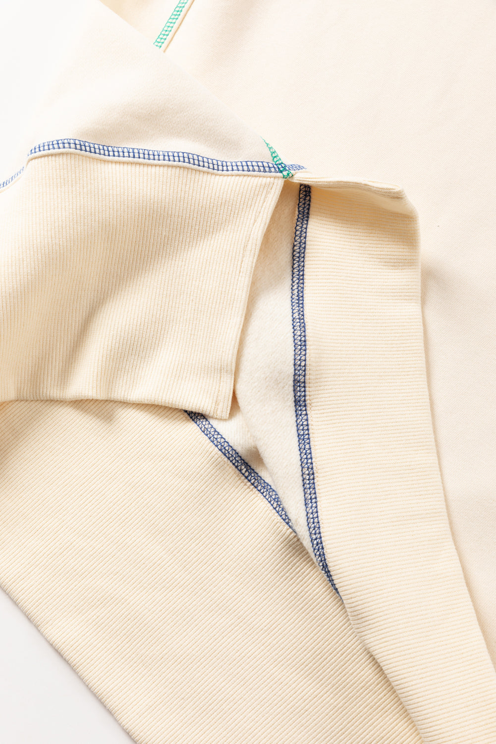 A woman with blonde hair is facing away, wearing a Contrast Stitching Split Baggy Sweatshirt. She stands in a room adorned with plants and wooden furniture in the background.