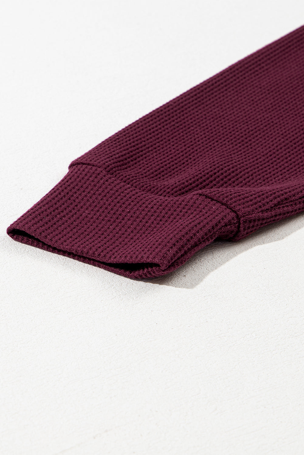 A woman in a Red Dahlia Waffle Knit Fleece Lined High Low Oversized Hoodie and black shorts is seen from behind, standing against a plain gray background.