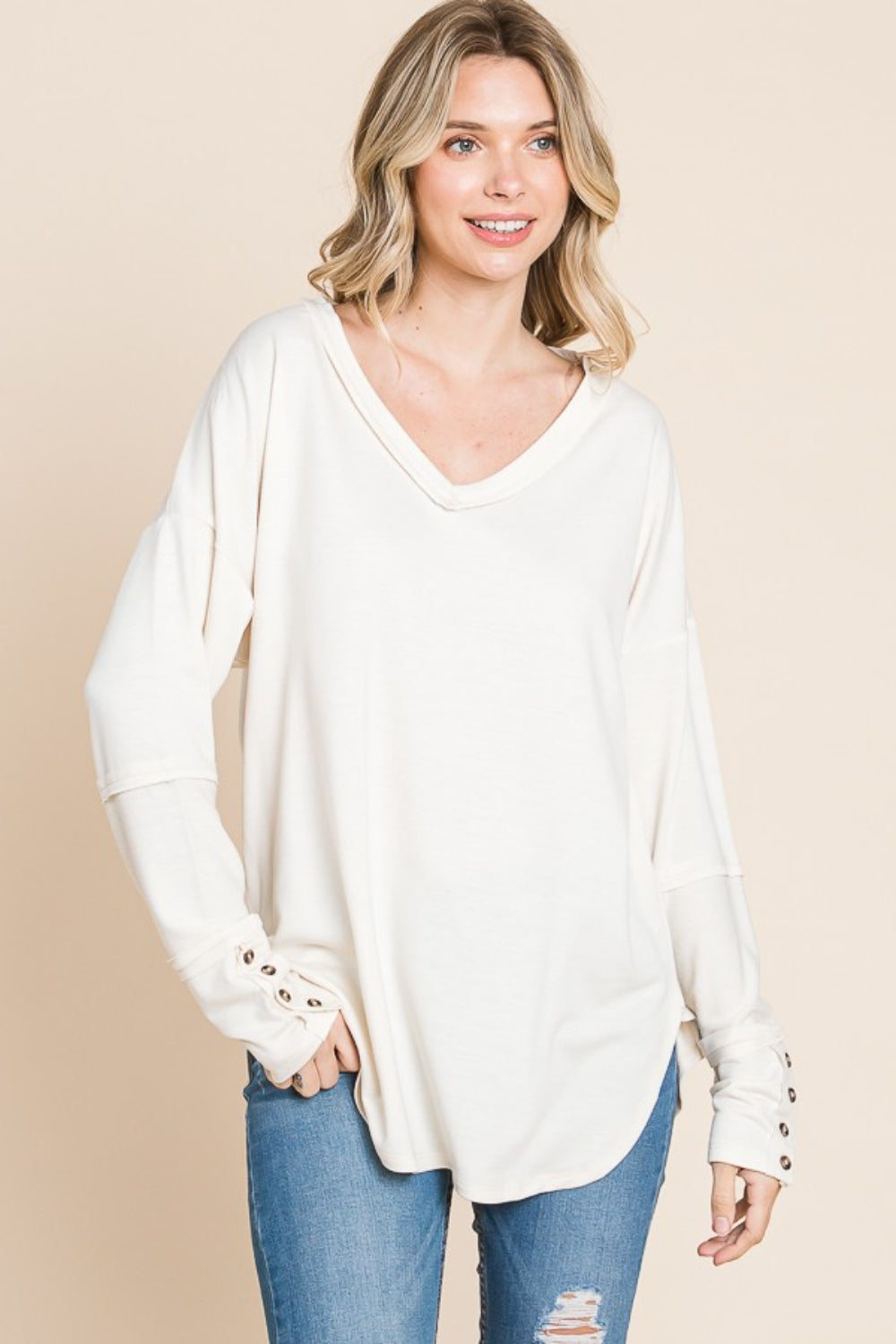 A person wearing the Culture Code Full Size V-Neck Dropped Shoulder Blouse, crafted from breathable fabric, poses against a beige background, highlighting the button details on the sleeves.