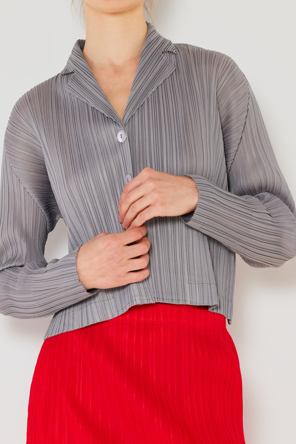 A person wearing the Marina West Swim Pleated Cropped Button Up Shirt in teal, complete with long sleeves and a matching skirt, stands against a light background, adding a modern touch to the classic pleats.