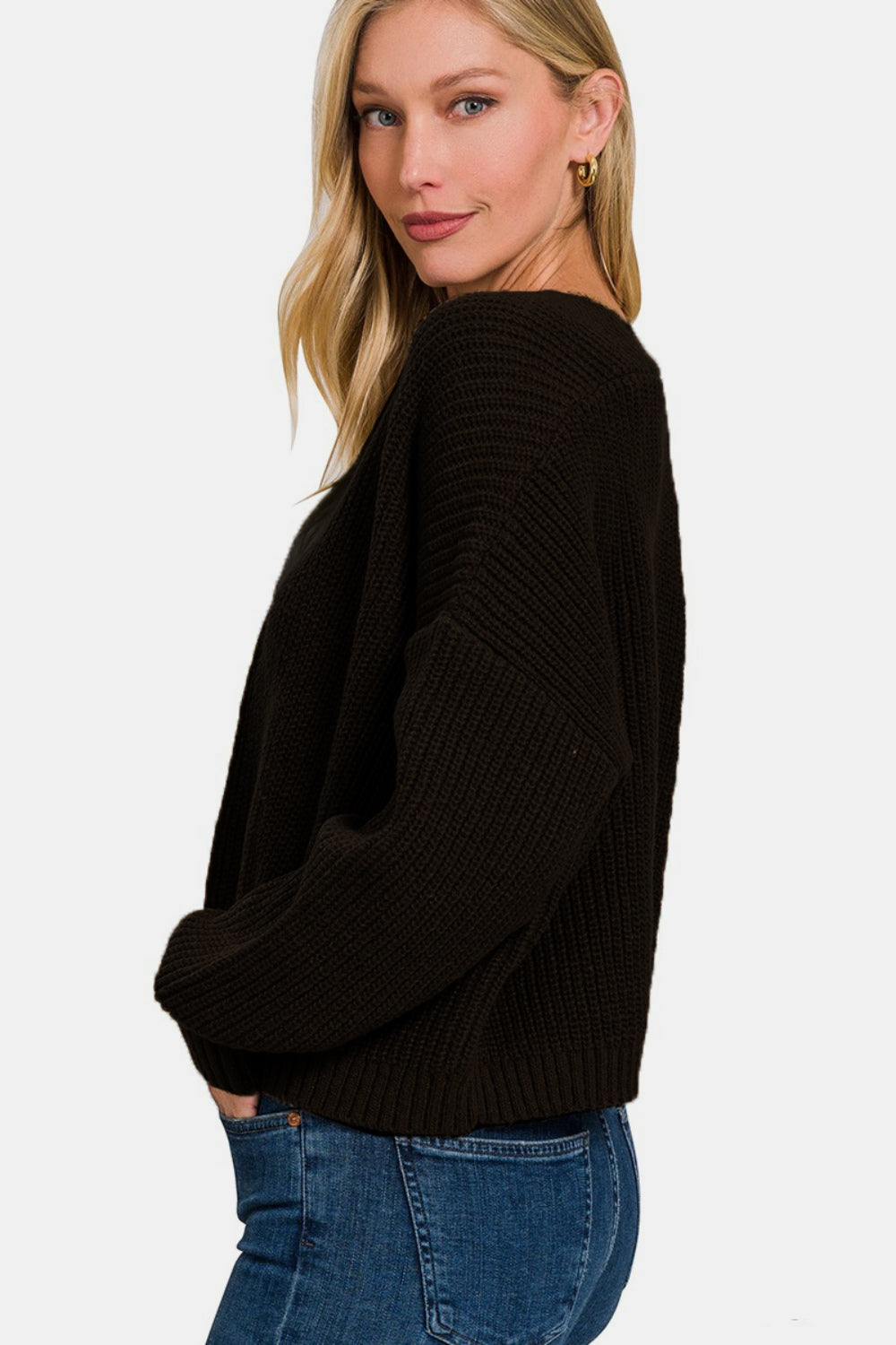 A person with long blonde hair wearing a black Zenana Open Front Drop Shoulder Sweater Cardigan, a white top, and blue jeans poses against a plain background.