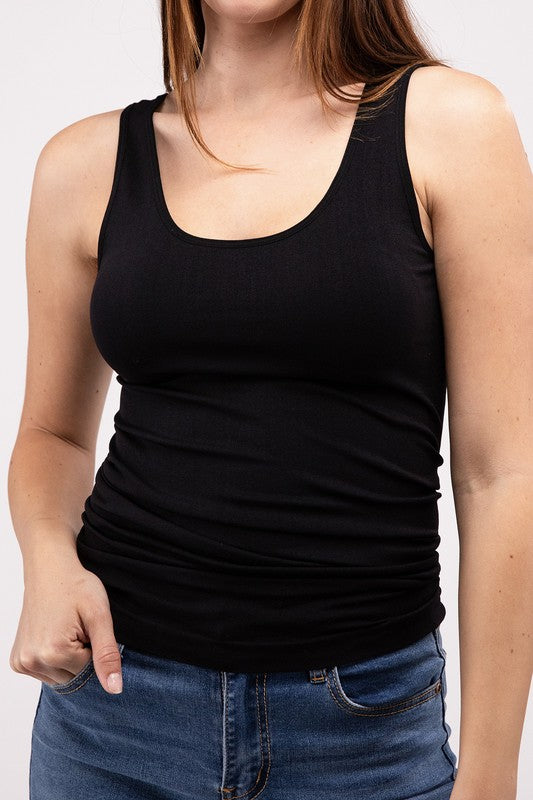 A woman in a white Front & Back 2-Way V-Neck Seamless Tank and black pants, standing with hands on hips and looking at the camera.