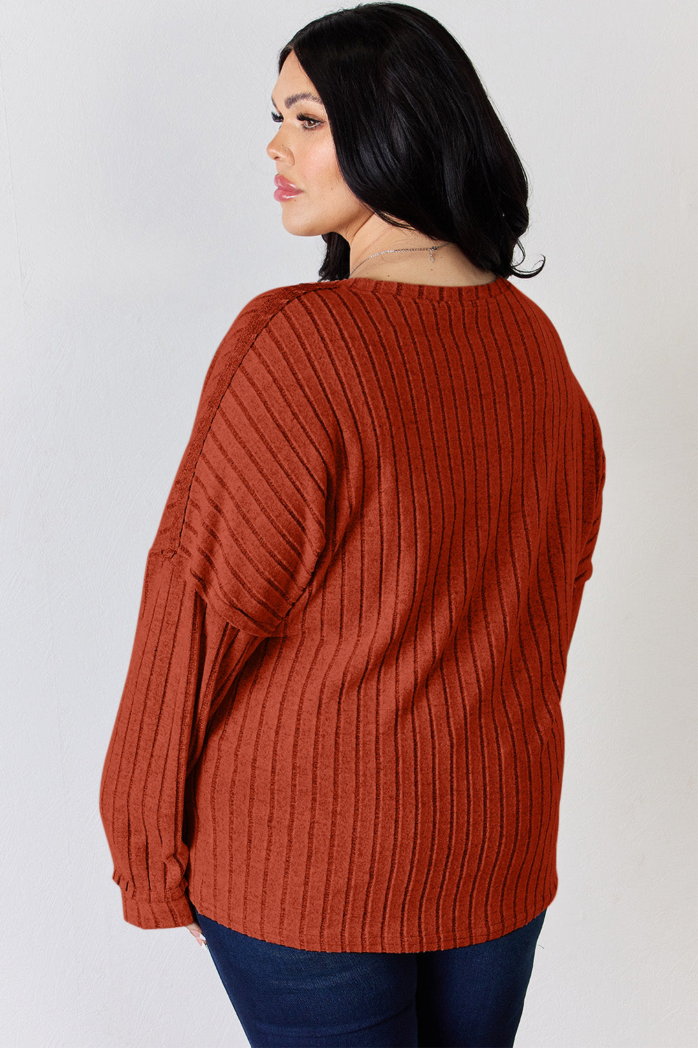 A woman with long, wavy blonde hair wears a slightly stretchy, textured Basic Bae Full Size Ribbed Half Button Long Sleeve T-Shirt in pink, standing against a neutral backdrop.