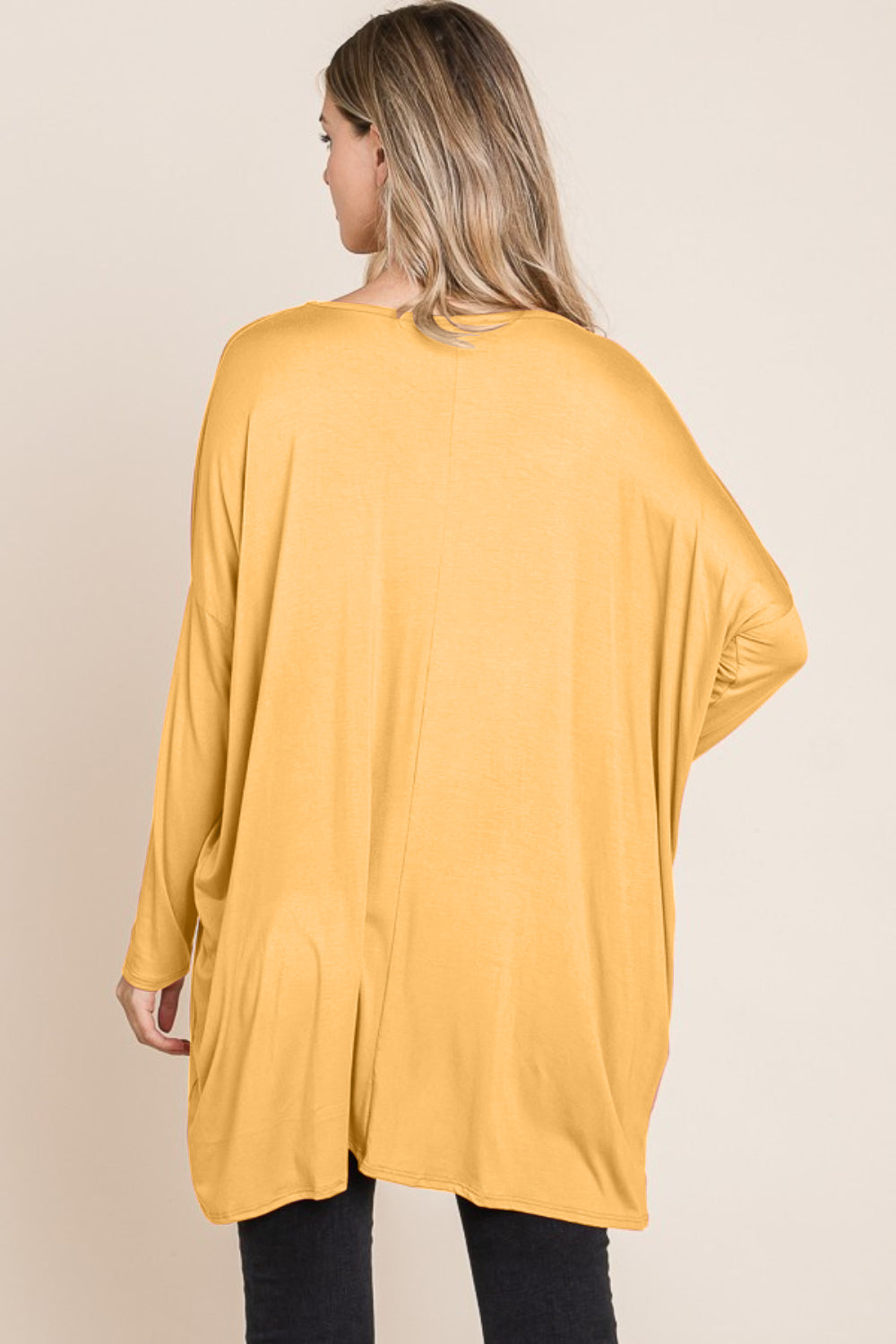 A woman with long blonde hair is wearing a versatile and comfortable, loose-fitting BOMBOM Round Neck Long Sleeve Oversized Top in yellow and blue jeans. She is smiling and standing against a plain light background.