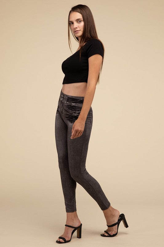 A person wearing Denim Leggings in a high-waisted black design and paired with black heels poses against a plain beige background, highlighting the sleek, stretchy fit.