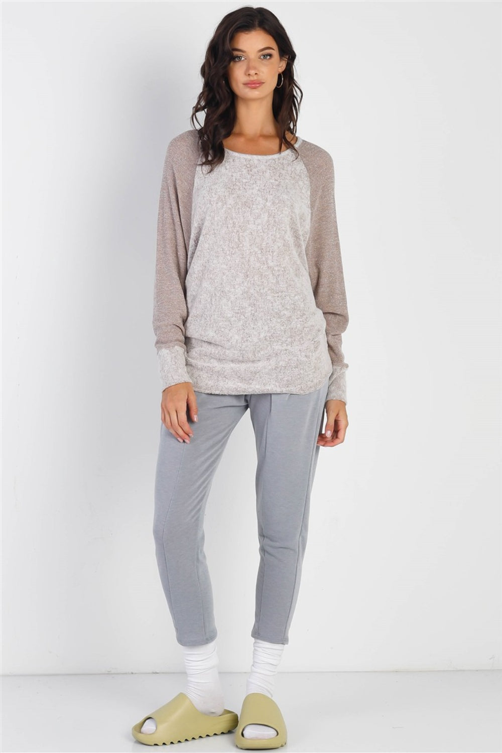 A woman stands wearing the Cherish Apparel Round Neck Long Sleeve Contrast Top in pink and gray with matching gray pants, set against a plain background.