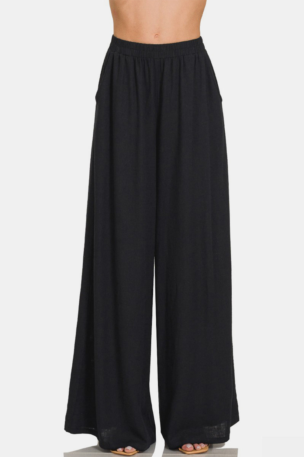 A person wearing Zenana Pleated Linen Blend Wide Leg Pants with an elastic waistband. The chic addition of these wide-leg silhouette pants is evident, even though the image is cropped at the torso and feet.