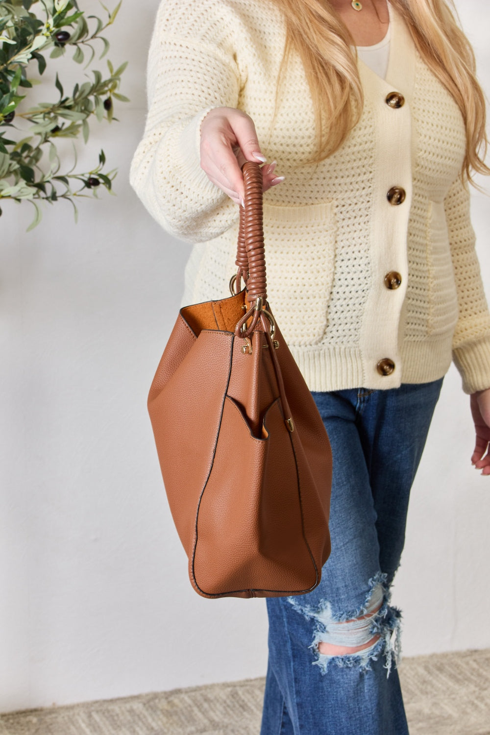 Effortlessly displaying the SHOMICO Faux Leather Handbag with Pouch, which features a spacious design in brown with gold accents and a woven handle, this piece exemplifies versatility. Paired with a cream sweater and blue jeans, its minimalist style perfectly balances fashion and function.