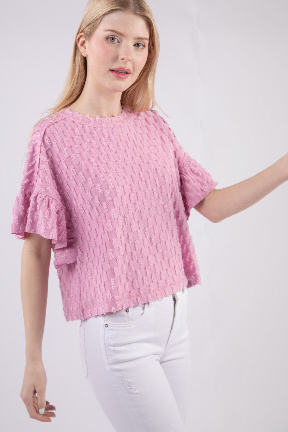 Person wearing the VERY J Full Size Texture Ruffle Short Sleeve Top, a chic and feminine textured pink blouse, paired with white pants, standing against a plain background.