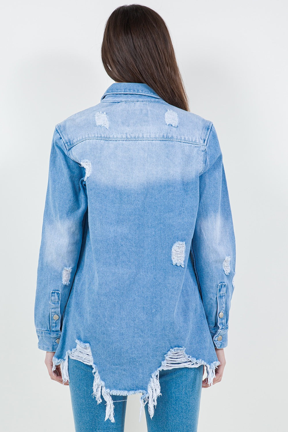 A woman stands against a plain background wearing the American Bazi Raw Hem Distressed Long Sleeve Denim Jacket over a white crop top and ripped jeans, adding an edgy flair to her wardrobe.