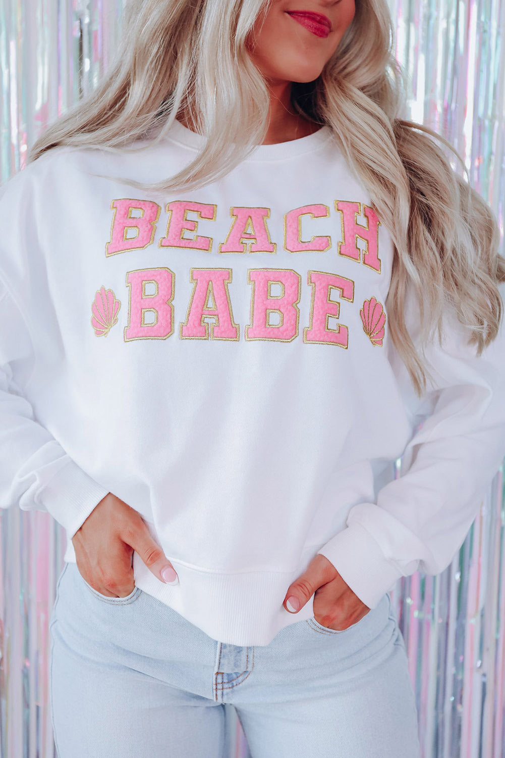 A person with long blonde hair is standing with their back to the camera, wearing a White BEACH BABE Slogan Graphic Casual Sweatshirt and light blue jeans.