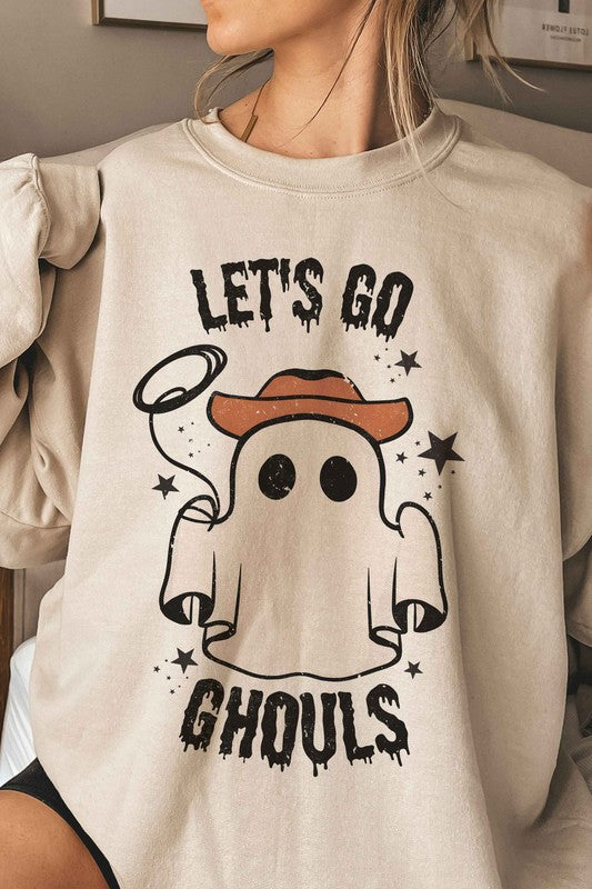 Individual adorned in a LETS GO GHOULS Graphic Crewneck, characterized by a beige hue and featuring a ghost donning a cowboy hat along with the text "Let's Go Ghouls.