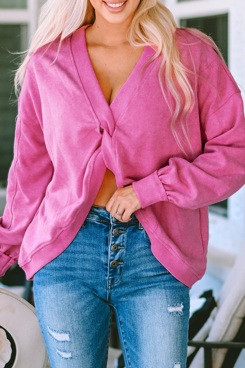 A woman stands with her back to the camera, wearing a long-sleeved Rose Exposed Seam Twist Open Back Oversized Sweatshirt and light blue jeans, showcasing a relaxed fit.