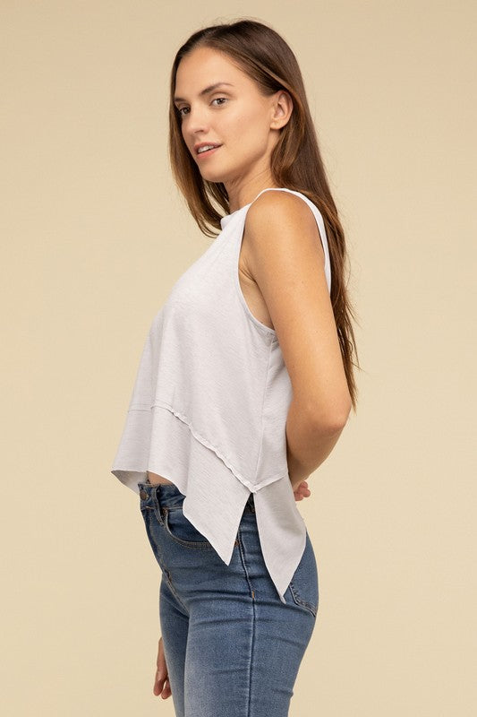 Wearing the Shark Bite Side Slit Short Sleeveless Top in maroon paired with white pants, a model is set against a beige background, exemplifying an effortlessly chic and casual wardrobe.