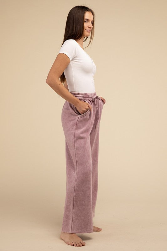 A person wearing acid wash fleece palazzo sweatpants with pockets paired with a white ribbed top, standing barefoot on a neutral background.