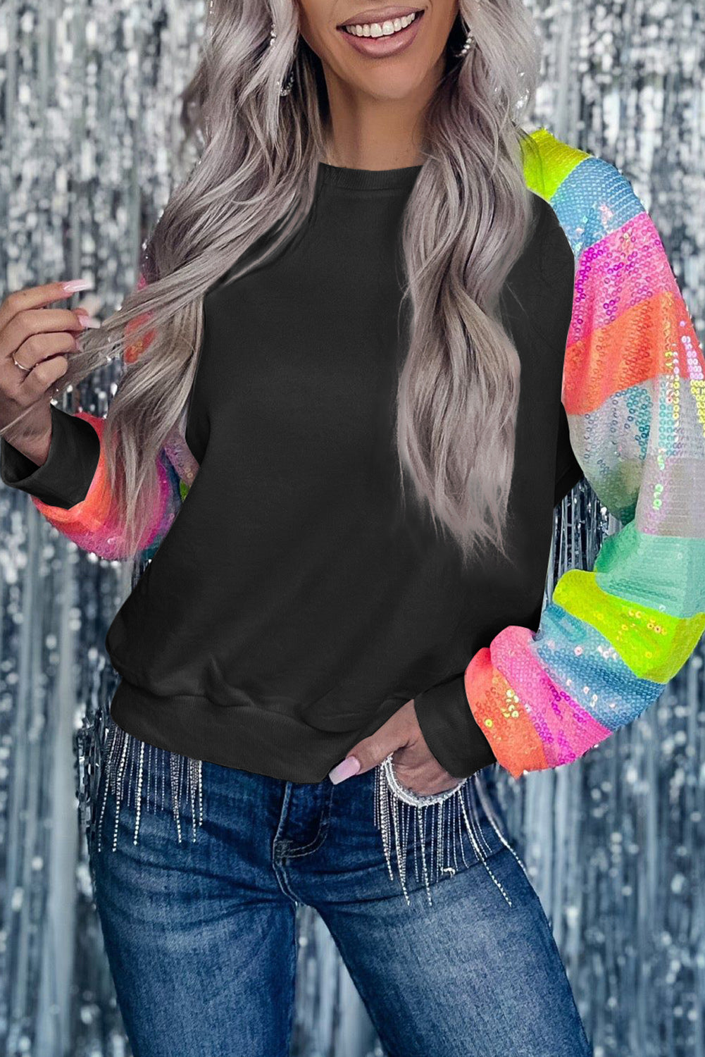 A person with shoulder-length hair is wearing a Black Sequin Color Block Raglan Sleeve Pullover Sweatshirt and blue jeans. They are facing away from the camera in a room with a potted plant.