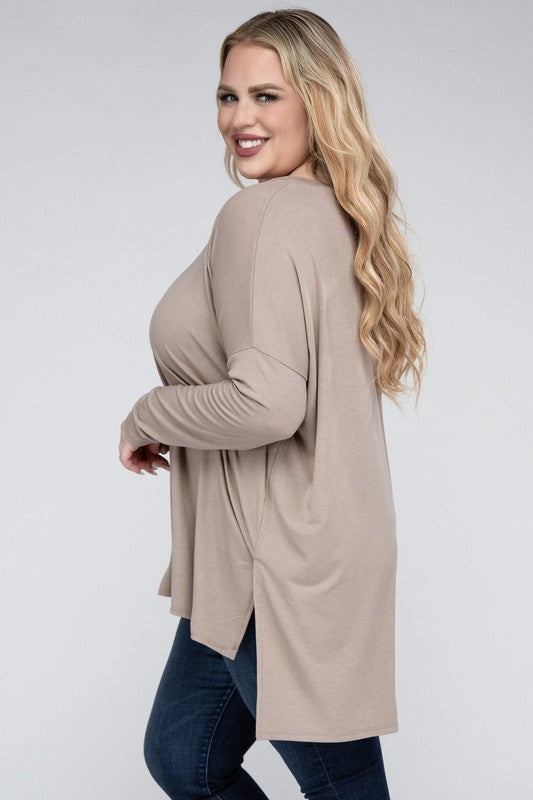 A woman with long, blonde hair wears a Plus Dolman Sleeve V-Neck Side Slit Hi-Low Hem Top and blue jeans, posing with one hand on her hip and smiling at the camera.