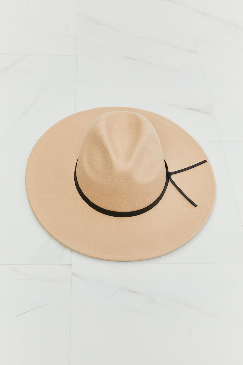 Wearing the Fame Make It Work Fedora Hat in light beige with faux leather detailing and a white tank top, a person smiles slightly while tilting their hat with one hand.