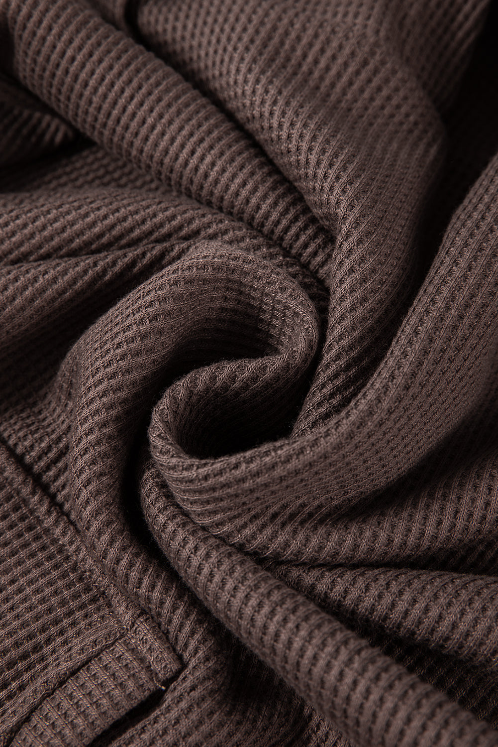 A woman with long hair is standing in profile, wearing a Coffee Waffle Knit Fleece Lined High Low Oversized Hoodie and black shorts. The background is a plain light gray.