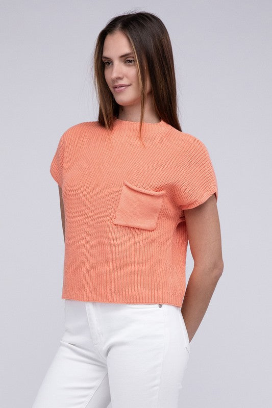 A woman in a JustFab mock neck short sleeve cropped sweater and white pants, smiling slightly, stands with one hand on her hip against a light grey background.