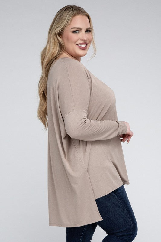 A woman with long, blonde hair wears a Plus Dolman Sleeve V-Neck Side Slit Hi-Low Hem Top and blue jeans, posing with one hand on her hip and smiling at the camera.